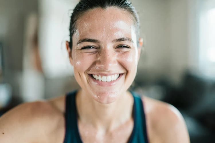 Mulher em close-up, suando após um treino intenso, com um sorriso satisfeito em uma sala de estar.